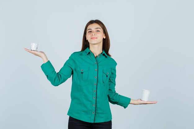 Señorita en camisa sosteniendo vasos de plástico de café y mirando complacido, vista frontal.