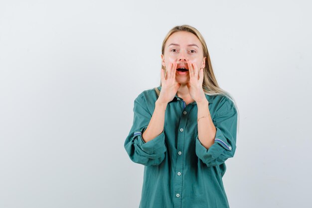 Señorita en camisa verde diciendo secretos con las manos cerca de la boca y mirando emocionado