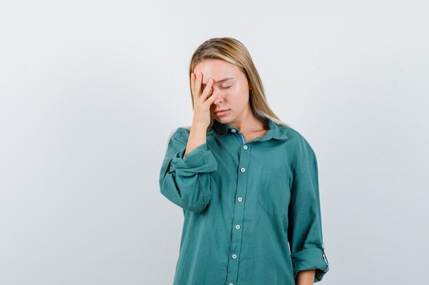 Señorita en camisa verde manteniendo la mano en la cara y con aspecto cansado