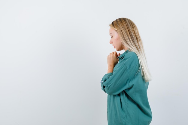 Señorita en camisa verde manteniendo las manos juntas mientras reza y mira esperanzada.