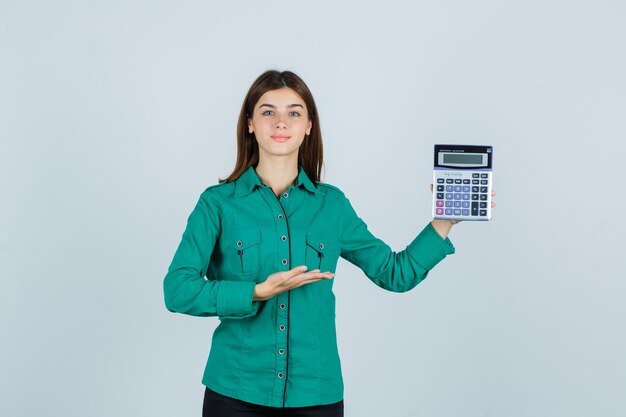 Señorita en camisa verde mostrando calculadora y mirando confiado, vista frontal.
