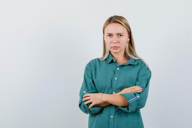 Señorita en camisa verde de pie con los brazos cruzados y con cara de tristeza