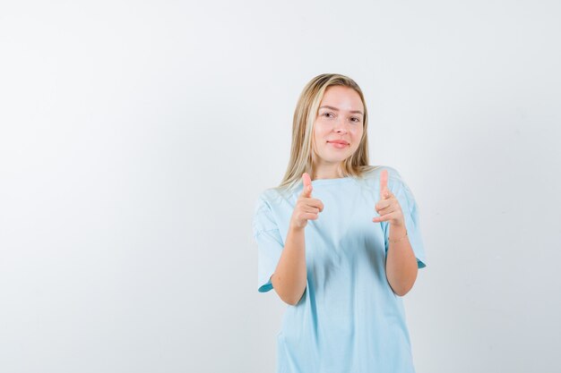 Señorita en camiseta apuntando a la cámara y mirando atractiva, vista frontal.