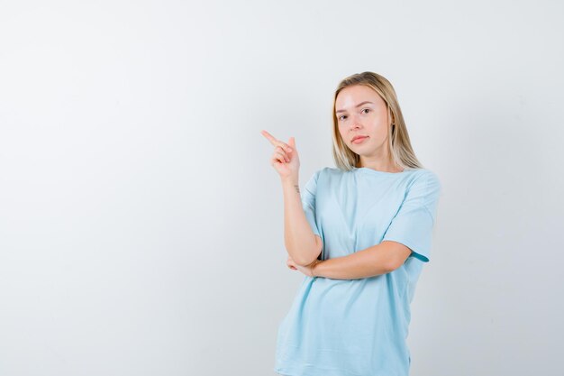 Señorita en camiseta apuntando a la esquina superior izquierda y mirando confiado aislado