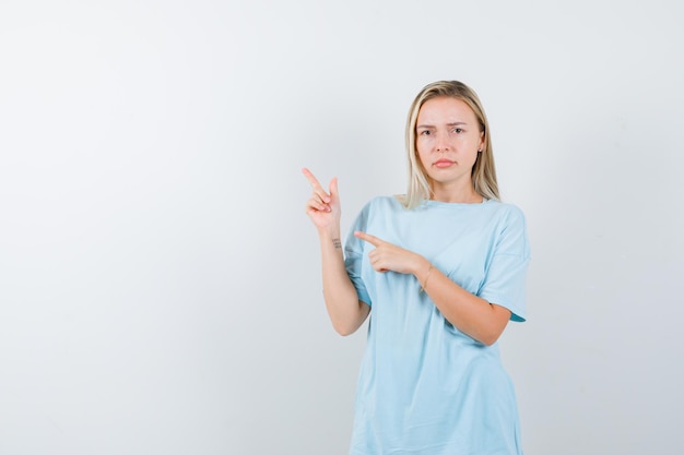 Señorita en camiseta apuntando a la esquina superior izquierda y mirando vacilante aislado