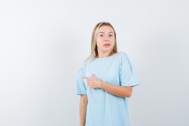 Señorita en camiseta apuntando hacia el lado izquierdo y mirando confiada, vista frontal.