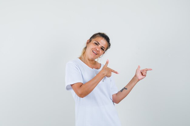 Señorita en camiseta apuntando hacia el lado y mirando alegre