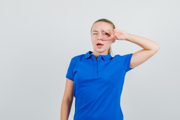 Señorita en camiseta azul que muestra el signo v en el ojo