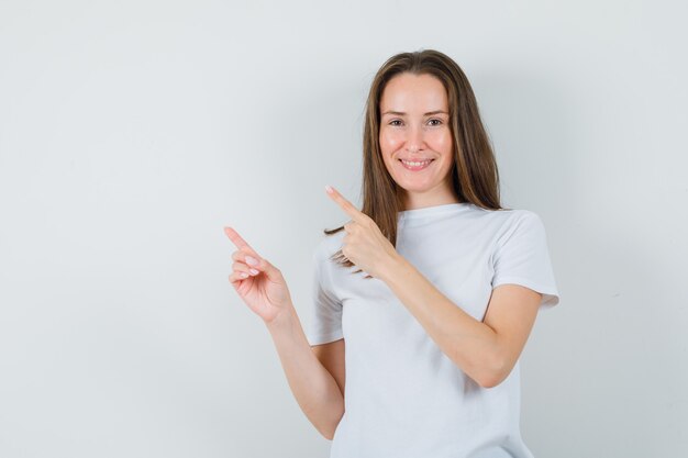 Señorita en camiseta blanca apuntando a la esquina superior izquierda y mirando confiada