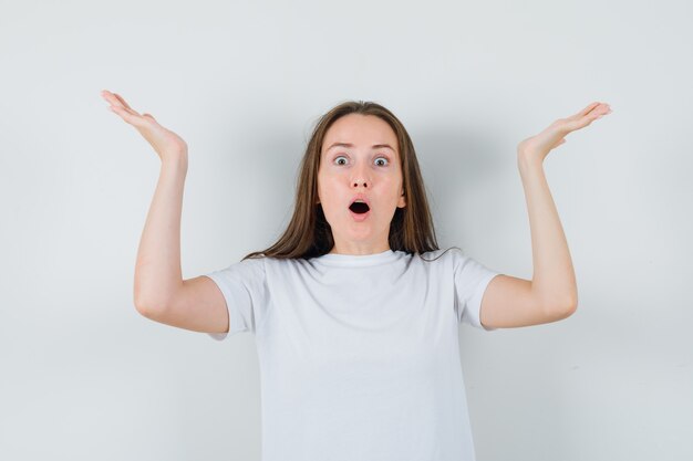 Señorita en camiseta blanca fingiendo sostener o levantar algo y mirando asombrado