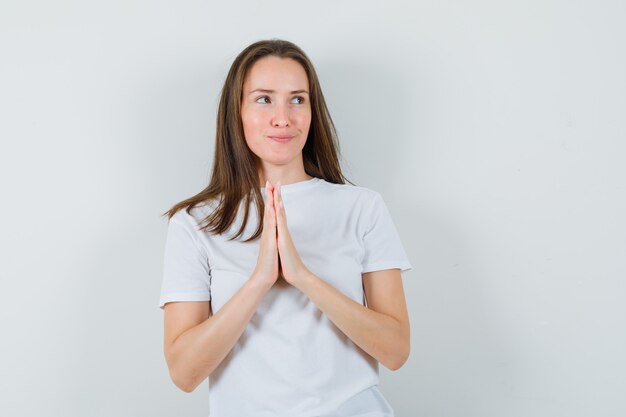 Señorita en camiseta blanca que muestra el gesto de namaste y parece esperanzada