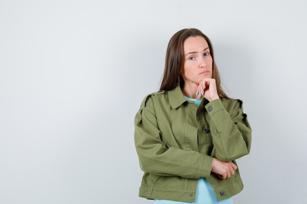 Señorita en camiseta, chaqueta apoyando la barbilla en el puño y mirando confiada, vista frontal.