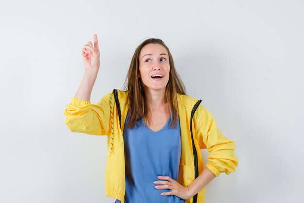 Señorita en camiseta, chaqueta apuntando hacia arriba y mirando esperanzada, vista frontal.