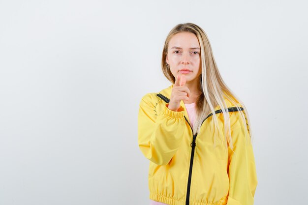 Señorita en camiseta, chaqueta apuntando a la cámara y mirando confiada