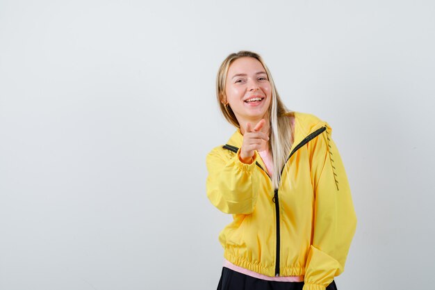 Señorita en camiseta, chaqueta apuntando a la cámara y mirando optimista