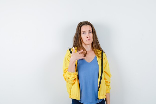 Señorita en camiseta, chaqueta apuntando a sí misma, labios curvados y mirada inocente, vista frontal.