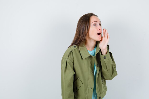 Señorita en camiseta, chaqueta gritando algo con la mano y mirando seria, vista frontal.