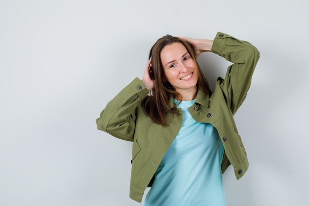 Señorita en camiseta, chaqueta con las manos en la cabeza y mirando alegre, vista frontal.