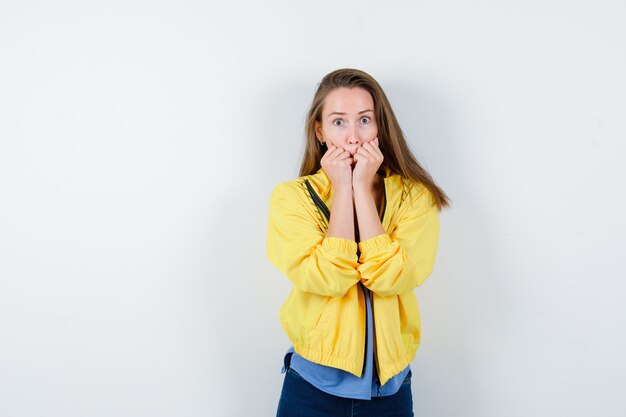 Señorita en camiseta, chaqueta mordiendo sus puños emocionalmente y mirando asustada, vista frontal.