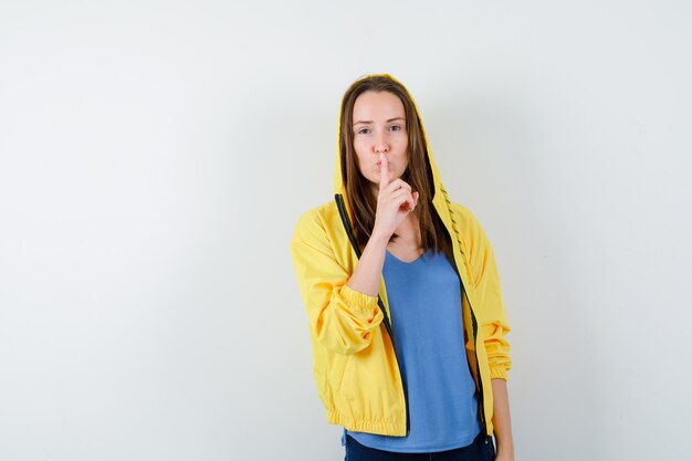 Señorita en camiseta, chaqueta mostrando gesto de silencio y mirando confiado, vista frontal.