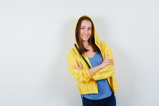 Señorita en camiseta, chaqueta de pie con los brazos cruzados y mirando alegre, vista frontal.