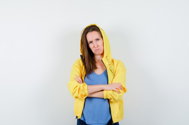 Señorita en camiseta, chaqueta de pie con los brazos cruzados y mirando molesto, vista frontal.