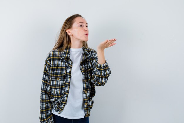 Señorita en camiseta, chaqueta soplando aire beso con labios fruncidos y luciendo linda vista frontal.