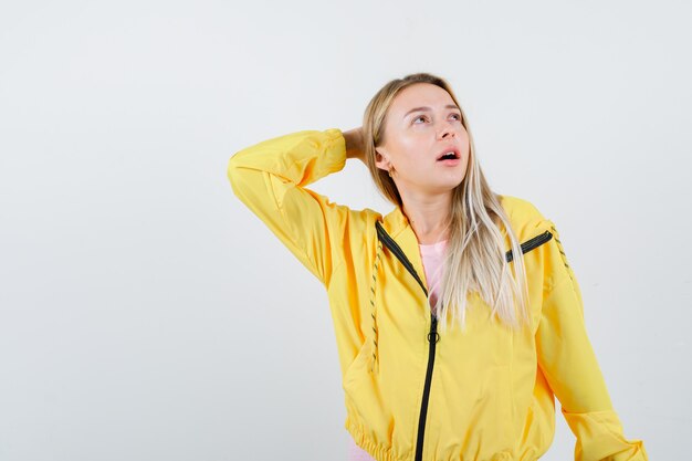 Señorita en camiseta, chaqueta sosteniendo la mano detrás de la cabeza y mirando asombrado