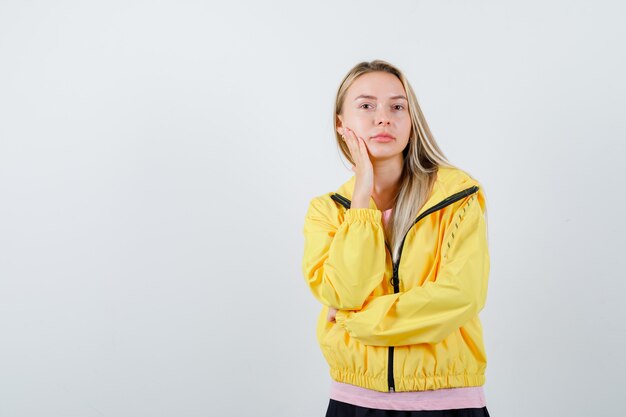 Señorita en camiseta, chaqueta sosteniendo la mano en la mejilla y luciendo atractiva