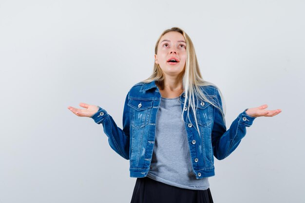 Señorita en camiseta, chaqueta vaquera, falda extendiendo las palmas para rezar y luciendo esperanzada