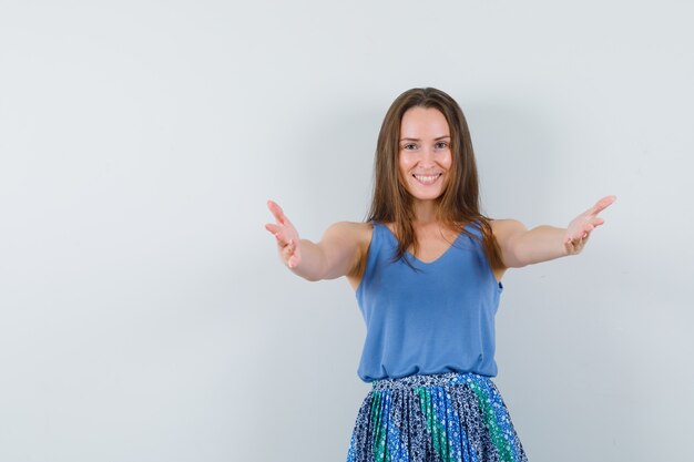 Señorita en camiseta, falda abriendo los brazos para abrazar y luciendo optimista, vista frontal.