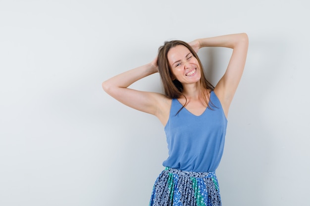 Foto gratuita señorita en camiseta, falda cogidos de la mano detrás de la cabeza y mirando relajado, vista frontal.