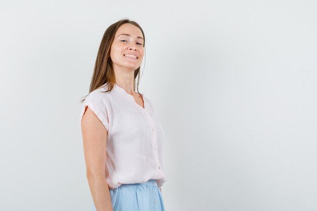 Señorita en camiseta, falda mirando a cámara y mirando alegre, vista frontal.