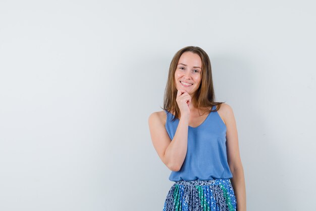 Señorita en camiseta, falda de pie en pose de pensamiento y mirando alegre, vista frontal.