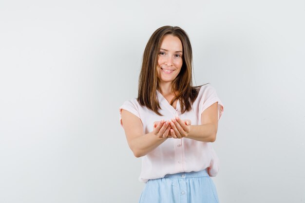 Señorita en camiseta, falda sosteniendo las manos ahuecadas y sonriendo, vista frontal.