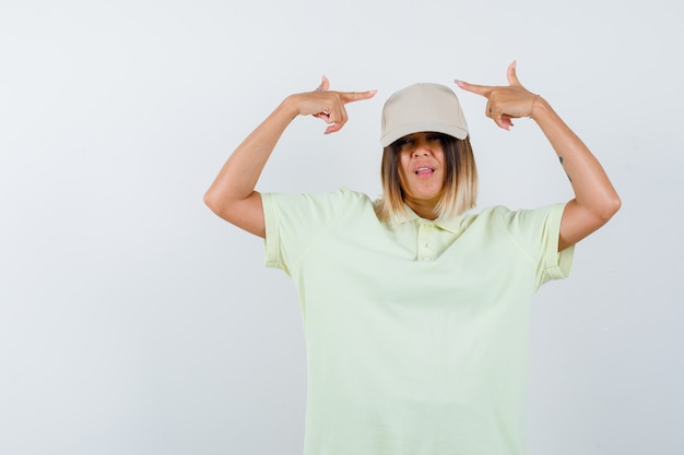 Señorita en camiseta, gorra apuntando a ambos lados y mirando confiada, vista frontal.