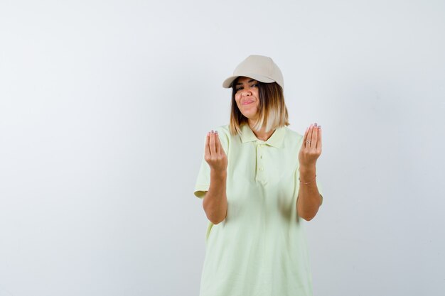 Señorita en camiseta, gorra mostrando gesto italiano y mirando encantada, vista frontal.