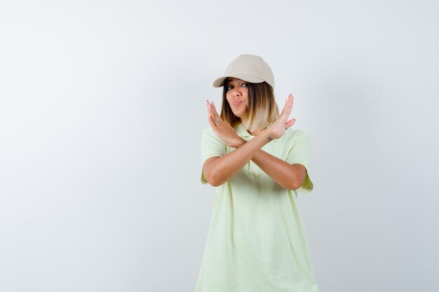 Señorita en camiseta, gorra mostrando gesto de parada mientras hace pucheros con los labios y mira confiada, vista frontal.