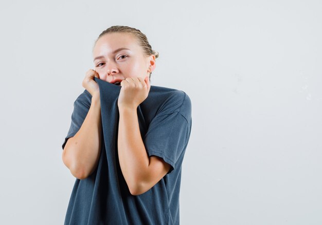 Señorita en camiseta gris tirando del cuello en la cara y mirando tímido