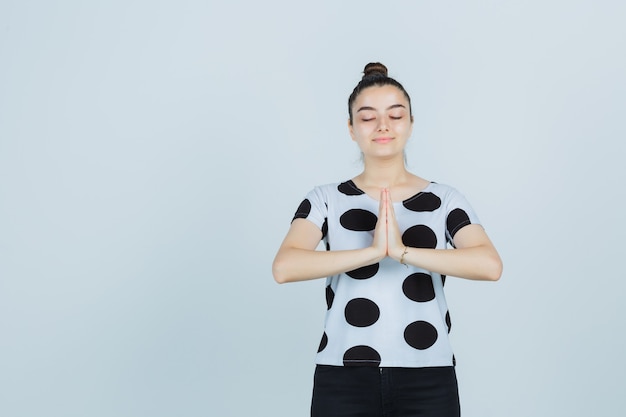 Foto gratuita señorita en camiseta, jeans mostrando gesto de namaste y mirando pacífica, vista frontal.