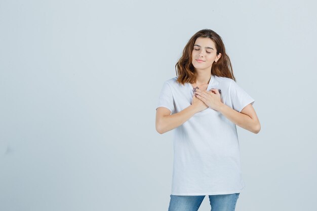 Señorita en camiseta, jeans mostrando gesto de oración y mirando esperanzado, vista frontal.