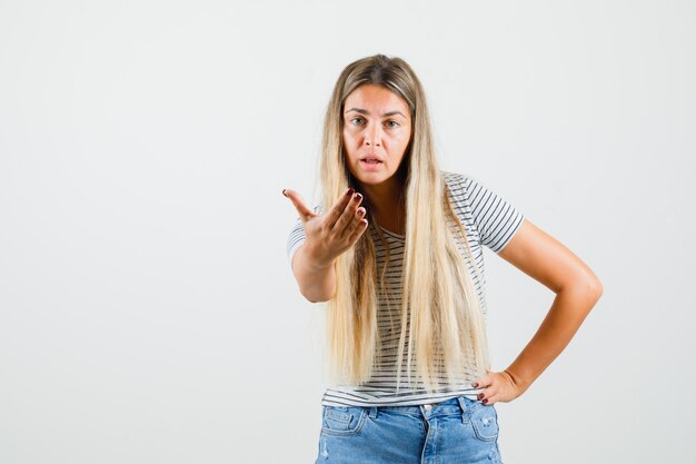 Señorita en camiseta levantando la mano en forma interrogativa y mirando concentrada, vista frontal.