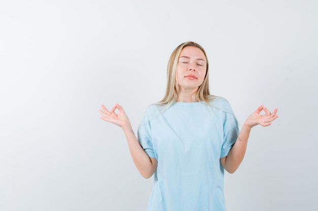 Señorita en camiseta mostrando gesto de meditación y mirando pacífica, vista frontal.