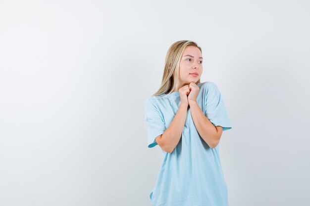 Señorita en camiseta mostrando las manos juntas en gesto de súplica y mirando esperanzado