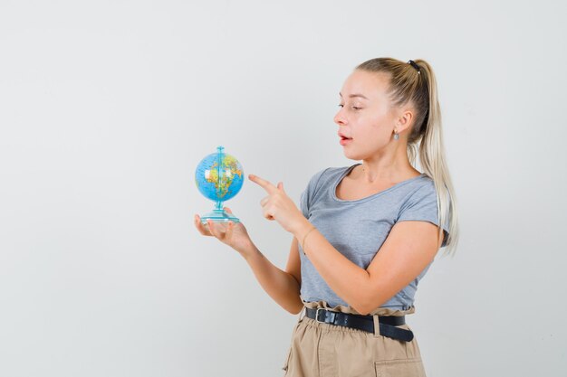 Señorita en camiseta y pantalón eligiendo destino en el mundo y mirando asombrado