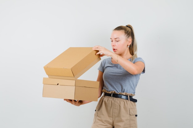 Señorita en camiseta y pantalón mirando por encima de cajas de cartón y mirando curioso