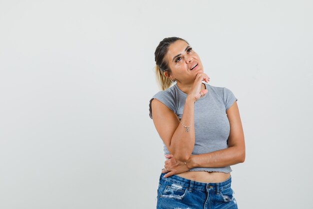 Señorita en camiseta, pantalones cortos apoyando la barbilla en la mano y mirando pensativo