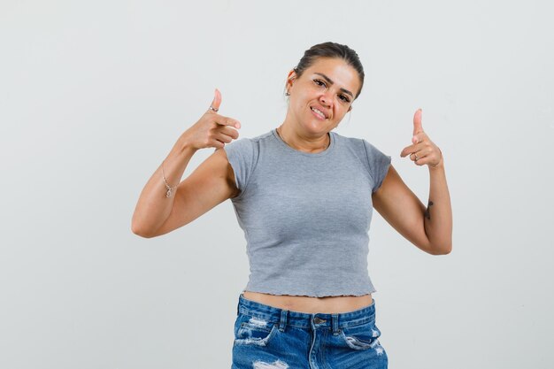 Señorita en camiseta, pantalones cortos apuntando a la cámara y mirando confiado