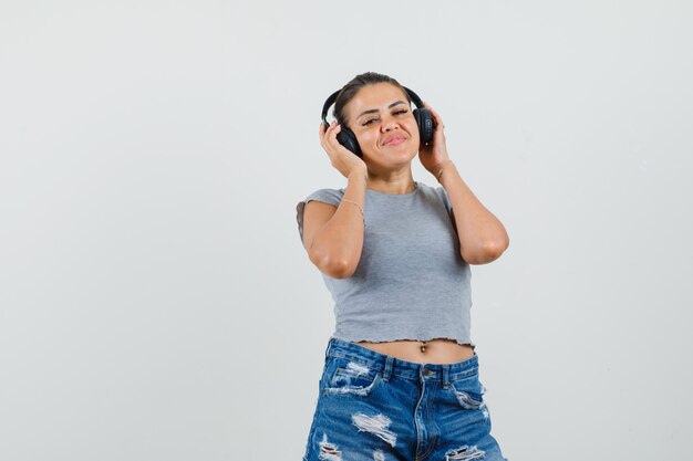 Señorita en camiseta, pantalones cortos disfrutando de la música con auriculares y mirando contento