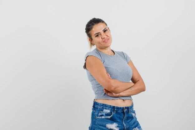 Señorita en camiseta, pantalones cortos de pie con los brazos cruzados y mirando alegre